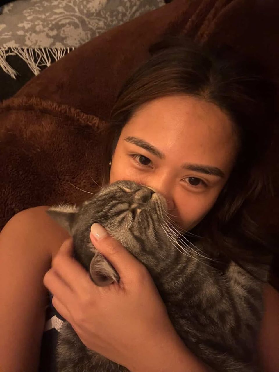 A woman cuddling her grey tabby cat cheek to cheek.